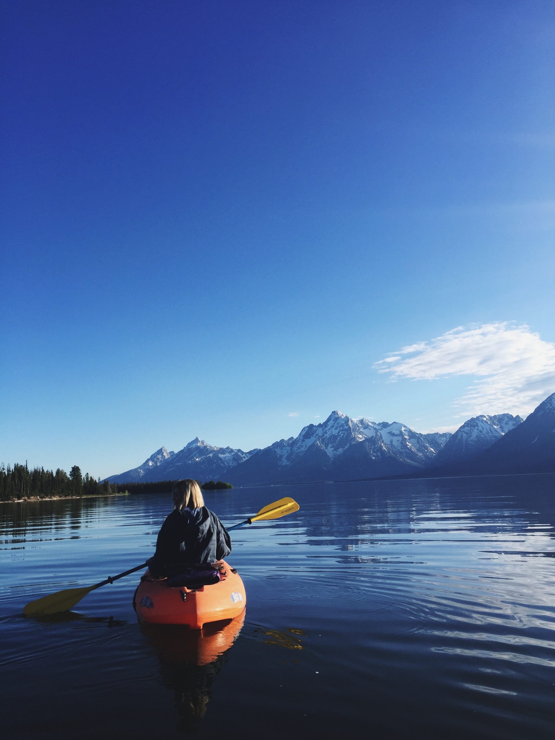 a woman kayaking on a large lake with mountains in the background on a clear day